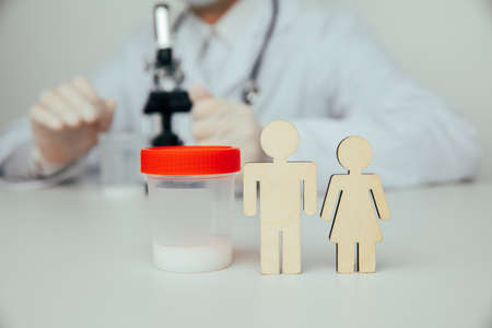 A plastic cup with sperm for semen analysis with a wooden couple. Planning pregnancy and health conceptの写真素材