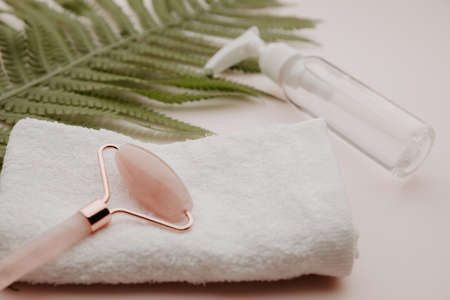 Roller on a towel and beauty product with a fern leaf on a pink backgroundの写真素材