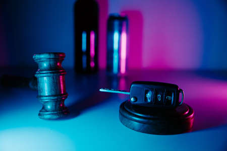 Car key, wooden gavel and alcohol drinks in neon light. Dangerous driving and lawの写真素材