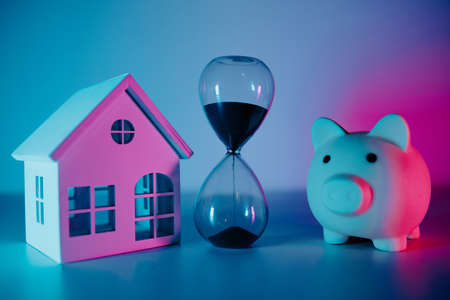 Hourglass and house model with piggy bank on the table close-upの写真素材