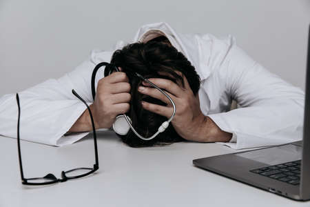 Tired depressed male doctor lays in medical office with a stethoscope on the table. Burnout conceptの写真素材