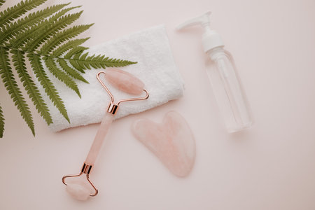 Essence in a bottle and roller, gua sha massage scraper on a pink background. Selfcare, beauty and health conceptの写真素材