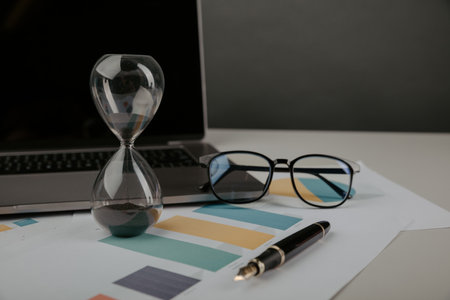 Hourglass on a workplace with reports. Time management conceptの写真素材