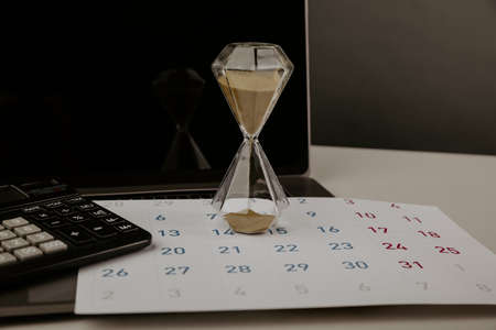 Hourglass on a desktop with calendar and laptop, deadline conceptの写真素材