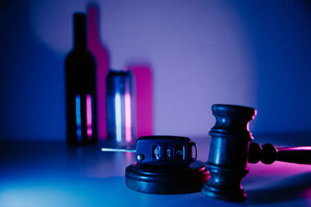 Car key, gavel and alcohol drinks in neon light. Dangerous drinking and drivingの写真素材