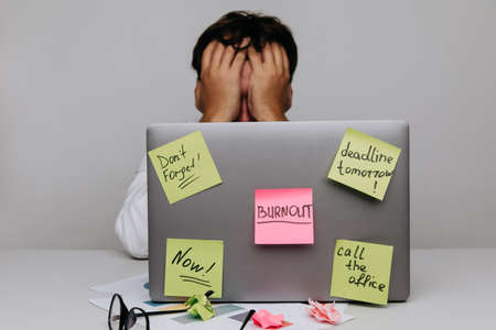Man hides in office. Worker have sticker pads on his laptop with tasksの写真素材