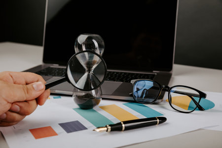 Hourglass, laptops and magnifier in man's hand. business concept.の写真素材