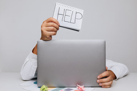 Overworked worker burying his head under a laptop asking for helpの写真素材