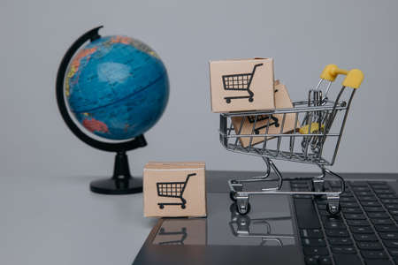 Paper boxes in a trolley on a keyboard and globe. Concept of online shopping.の写真素材