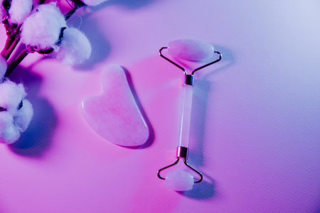 Skin care concept. Jade face roller for beauty facial massage therapy with fern leaf in neon lightの写真素材