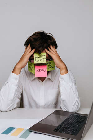 Burnout and overwork concept. Man office worker have sticker pads on his face with tasks. Vertical...
