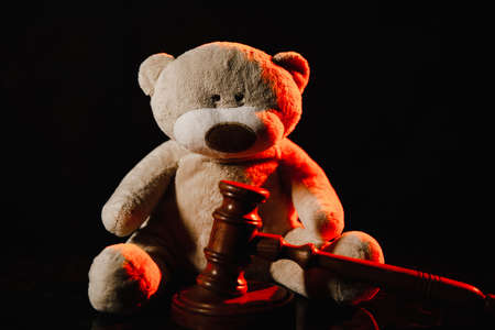 Wooden gavel and teddy bear as symbol of child in a dark court room. Law and children conceptの写真素材