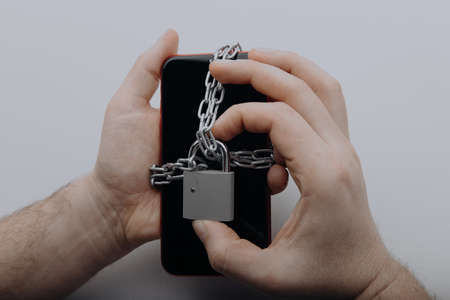 Information security or smartphone addiction concept. Smartphone with chain locked by padlock in mans handの写真素材