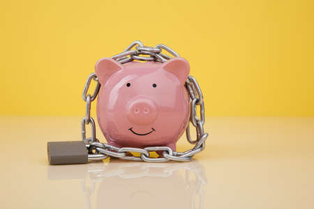Piggy bank with chain on yellow backgroundの写真素材