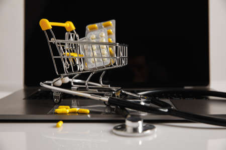 Online pharmacy. Trolley with medicines and stethoscope on a laptopの写真素材