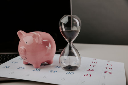 Hourglass with piggy bank on a calendar with laptop close-up. Online business conceptの写真素材