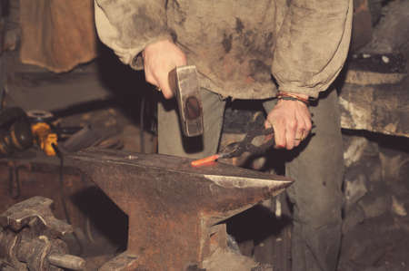 Blacksmith working metal with hammer on the anvil in the forge