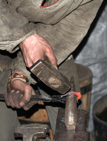 Blacksmith working metal with hammer on the anvil in the forgeの写真素材