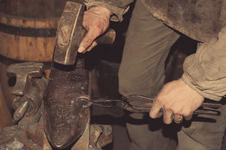 Blacksmith working metal with hammer on the anvil in the forge