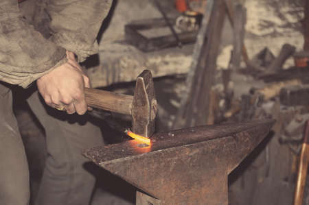 Blacksmith working metal with hammer on the anvil in the forgeの写真素材