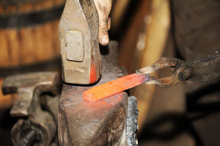 Blacksmith working metal with hammer on the anvil in the forge
