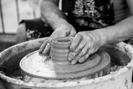 The potter makes pottery dishes on potter's wheel. The sculptor in workshop makes clay product closeup. Hands of the potter.の写真素材