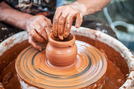 The potter makes pottery dishes on potter's wheel. The sculptor in workshop makes clay product closeup. Hands of the potter.の写真素材