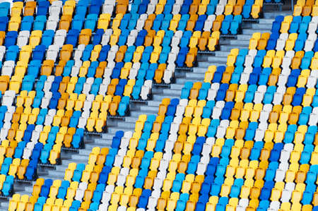 Blurred sitting fans colored plastic chairs at the football stadium background. Closeup of yellow...