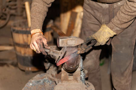Blacksmith working metal with hammer on the anvil in the forgeの写真素材
