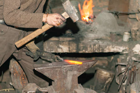 Blacksmith working metal with hammer on the anvil in the forgeの写真素材