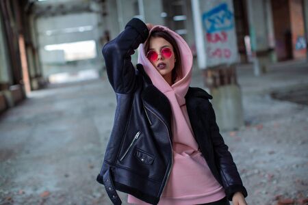 Beautiful young girl in powdery hoodie and biker jacket in underside spaceの写真素材