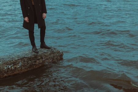 The silhouette of a man standing on the rocks by the choppy water.の写真素材