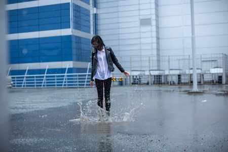 The girl jumps on a huge puddle.の写真素材