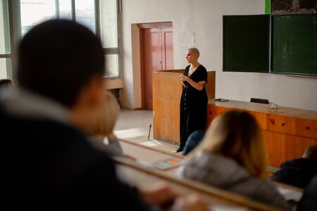 A woman teacher with short hair stands at the lectern and tells a lecture to her students.の写真素材