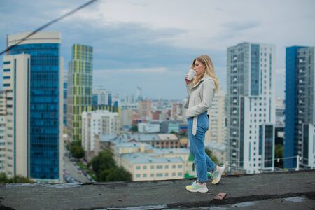 Young womandrinking coffee standing on the roof of the buildingの写真素材