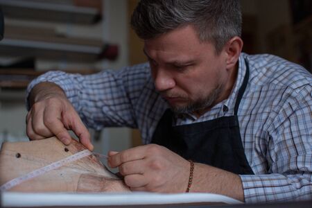 Portrait of a male shoemaker in a plaid shirt and apron at work