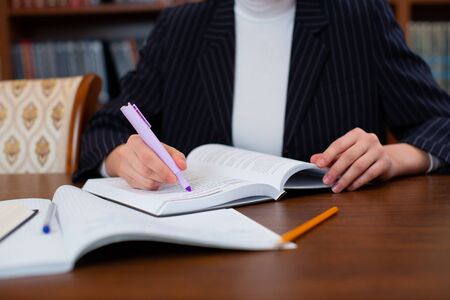 A student writes notes from books for homework in a library in a notebook