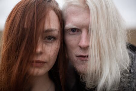 A young couple of red-haired girls and a guy with white hair staring intently at the camera floor of the face covered with hairの写真素材