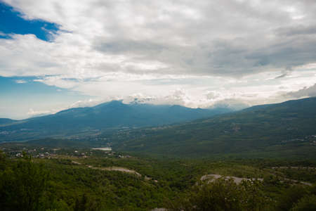 Crimean mountainous area under the sun on a murky day. Mountainous countryside at high noon. beautiful rural scenery with trees and fields on the rolling hills at the foot of the ridge.の写真素材