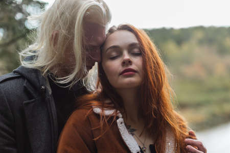 The unusual couple enjoying each others company against the backdrop of the forest. A boy in love albino whispers in the ear of a red-haired girl pleasant words.の写真素材