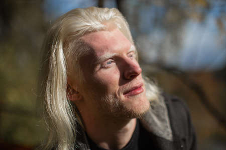 Photo in profile of a young man with a rare appearance of an albino with long hair and a beard, on...