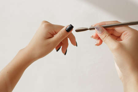 Well-groomed womens hands with an interesting manicure hold the tool for manicure photos on a beige background. High quality photoの写真素材