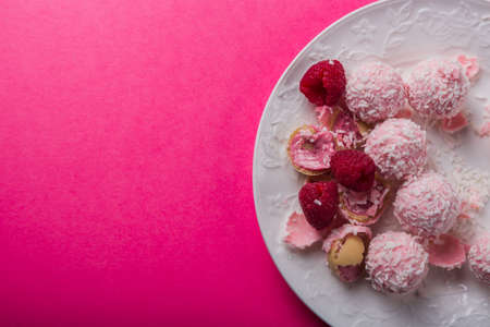 exquisite coconut candies lie on a white plate studded with raspberries on a bright pink colorful background. High quality photoの写真素材