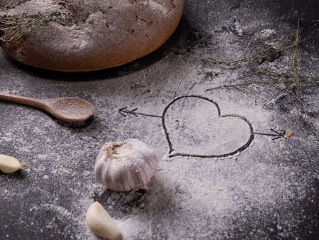 heart drawn on flour on a gray background near homemade garlic bread and spices. See the series of photos. Cook at home. homemade baking. High quality photoの写真素材