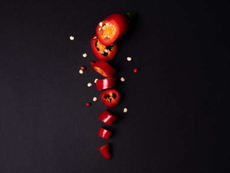 red fresh chili pepper on a black background cut into small pieces and grains of pepper. Photo of vegetables. High quality photoの写真素材