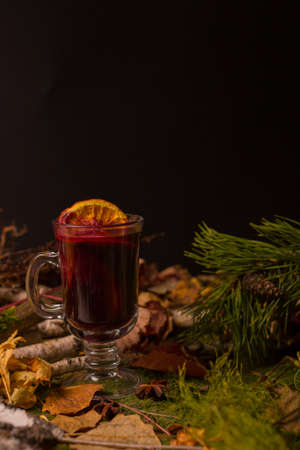 hot mulled wine drink in a glass against the background of spruce branches and dry leaves. New Years...