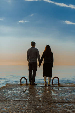 A couple in love guy and girl stand with their backs to the camera on the embankment by the sea,...
