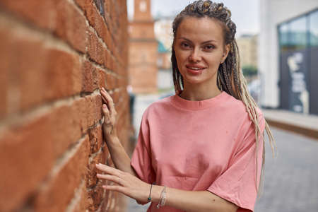 an informal girl with dreadlocks stands in the city against a brick wall, smiling and looking straight into the camera. High quality photoの写真素材