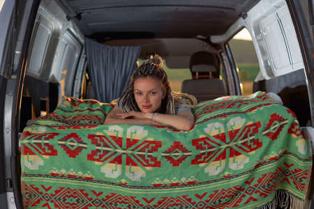 attractive girl lies in her minivan on a bright green blanket and looks directly into the camera....