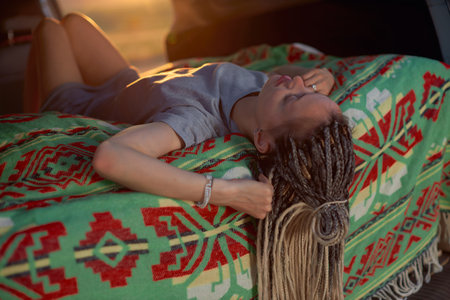 a girl with dreadlocks and a gray dress lies upside down on a bright green blanket in the car. High...